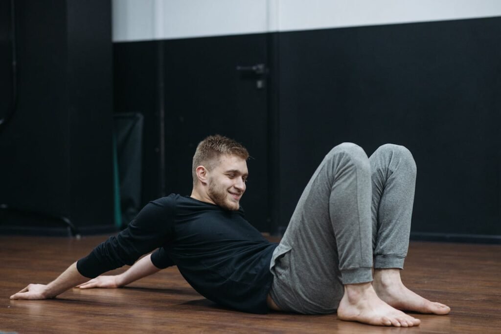 Young man performing a stretching and relaxation exercise on a gym floor.