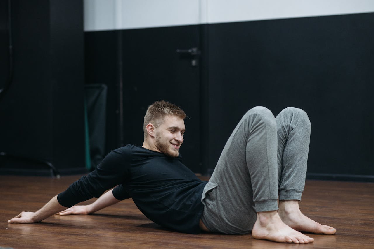 Young man performing a stretching and relaxation exercise on a gym floor.